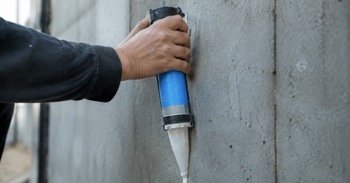 tube adhesif applique verticalement sur surface beton grise