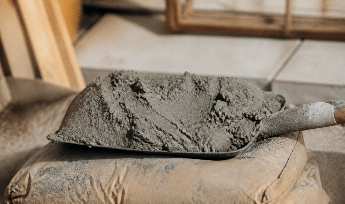 Pelle remplie de mortier gris posée sur sac de ciment